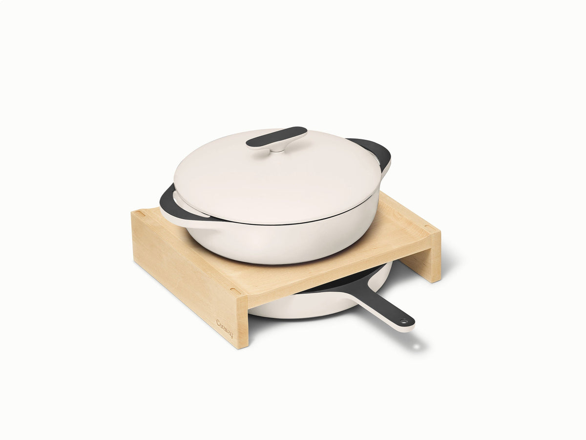 Caraway cream enameled cast iron braiser above a skillet on a wooden storage shelf.