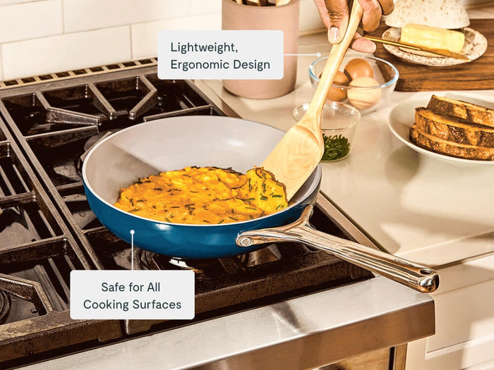 Hand using a wooden spatula to cook an omelet in a blue ceramic fry pan.