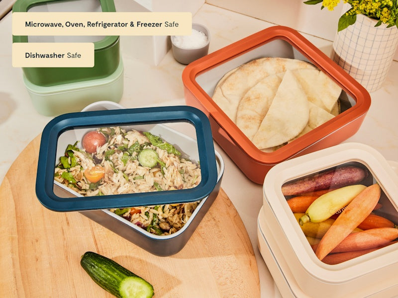 Caraway colorful ceramic food storage containers holding salad, bread, and cut vegetables with clear lids.