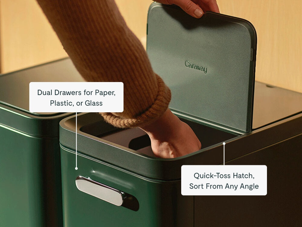 Person placing recyclables through the top hatch of a green two-drawer recycling bin.