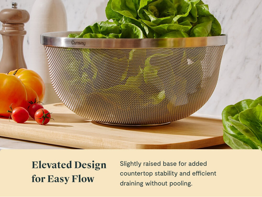 Caraway stainless steel mesh strainer holding lettuce on a wooden board.