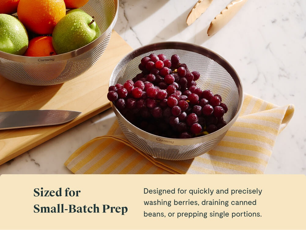 Caraway small stainless steel strainer holding grapes on a folded towel.