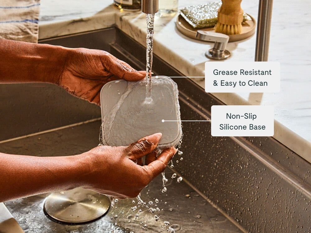 Hands rinsing a spoon rest under running water at a sink.