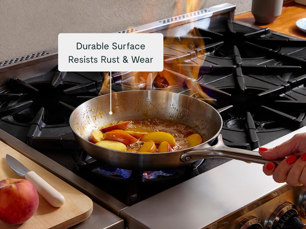 Caraway stainless steel fry pan flambéing fruit on a stove.