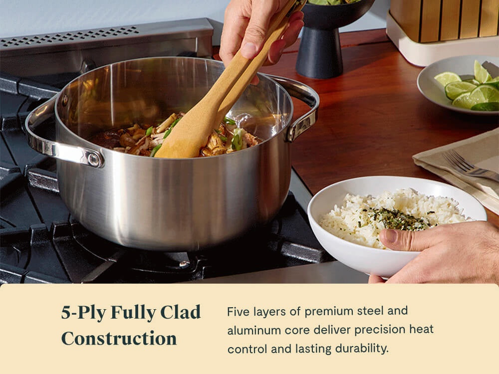 Hand stirring a cooked meal in a stainless steel Dutch oven beside a bowl of rice.