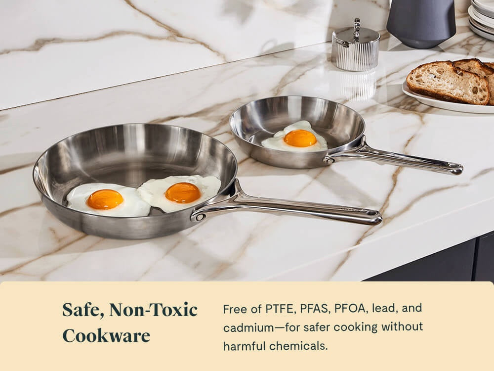 Two stainless steel fry pans holding fried eggs on a kitchen counter.