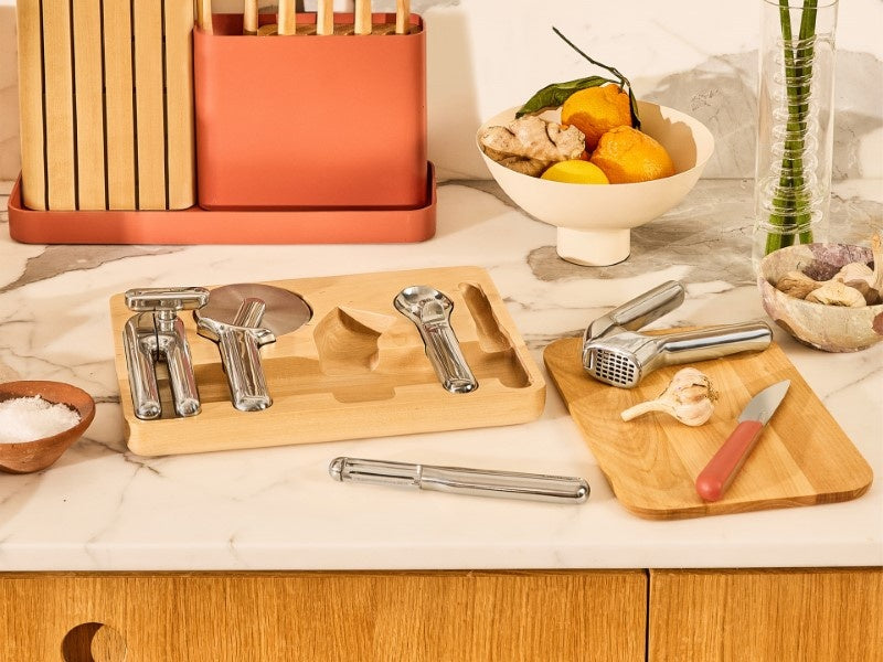 Caraway stainless steel kitchen gadgets in and beside a wooden drawer organizer on a kitchen counter.