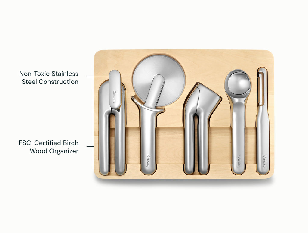 Caraway stainless steel can opener, pizza cutter, garlic press, ice cream scoop, and peeler in a wooden drawer organizer.
