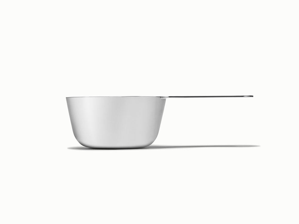 Caraway side view of a stainless steel measuring cup with a long flat handle.