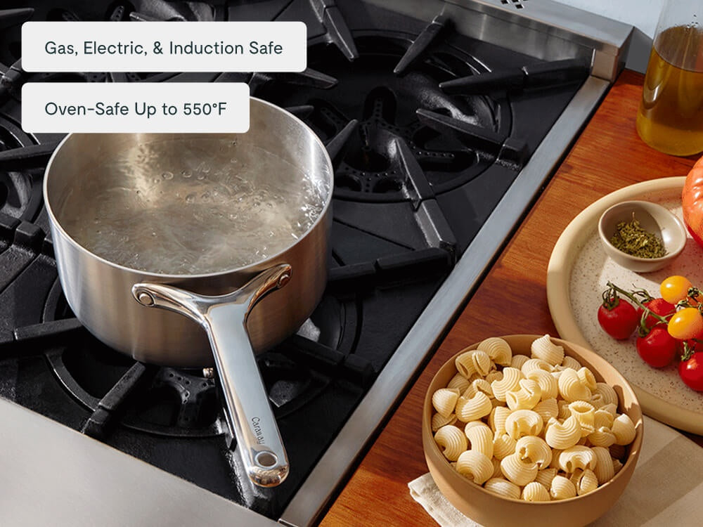 Water boiling in a stainless steel sauce pan beside uncooked pasta.