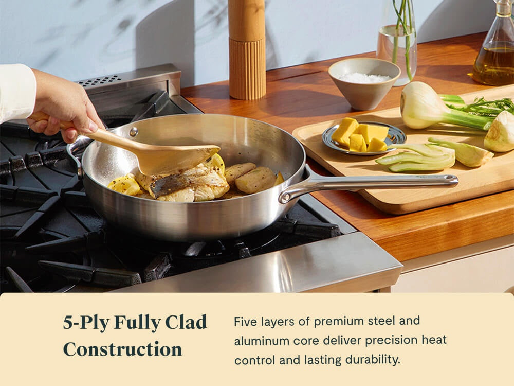 Hand turning food with a wooden utensil in a stainless steel sauté pan on a stove.