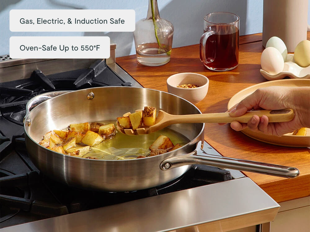 Hand serving cooked gnocchi from a stainless steel sauté pan on a stove.