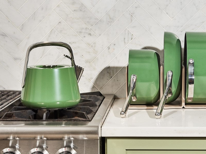 Caraway Sage whistling tea kettle beside a stove on a kitchen counter.