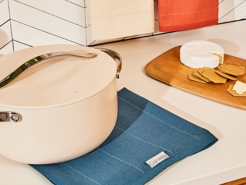Caraway cream Dutch oven resting on a Navy tea towel beside crackers and cheese.